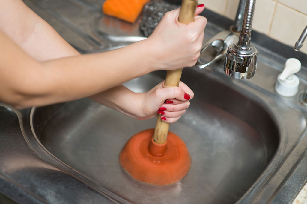 Woman trying to unclog a drain with a plunger. She needs drain cleaning services.